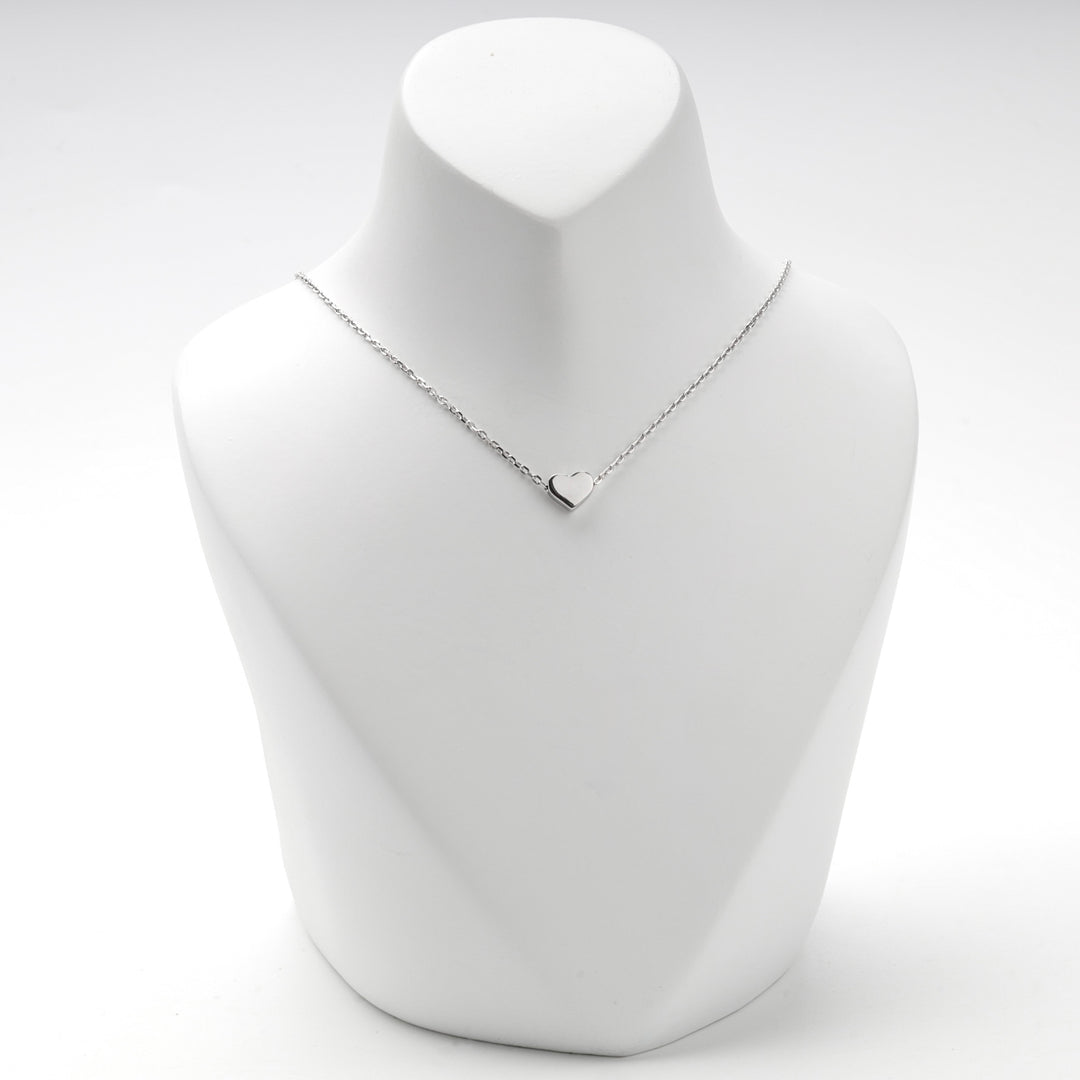 Small puffed silver heart sitting on the chain at the base of the neck