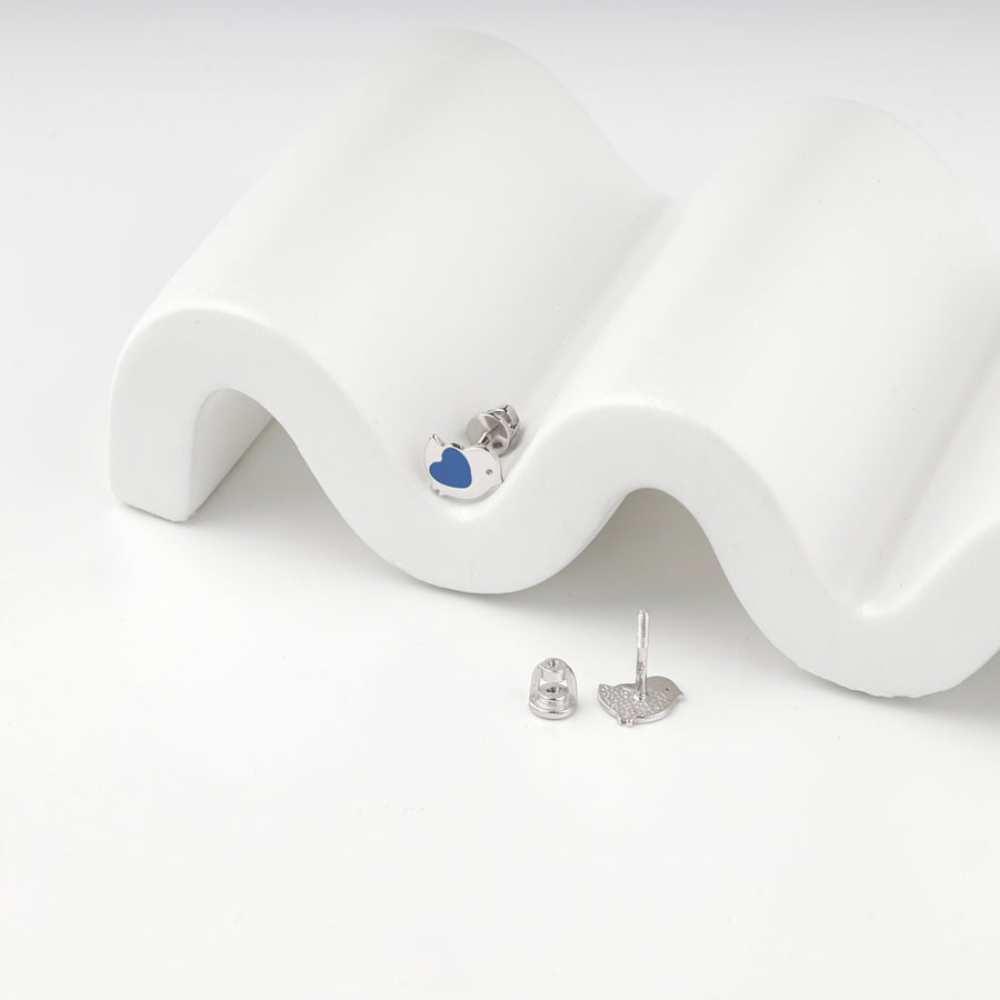 Blue enamel bird stud earring on a white wave display with the second earring beside it