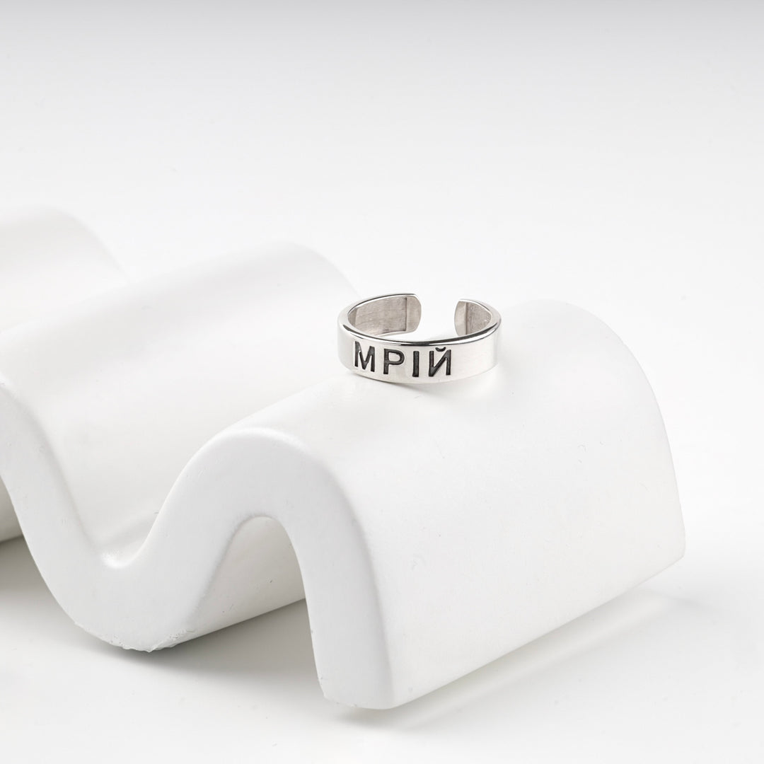 Engraved silver ring resting on a white wave display