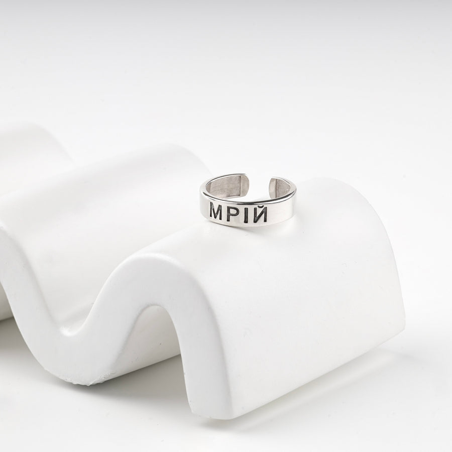 Engraved silver ring resting on a white wave display