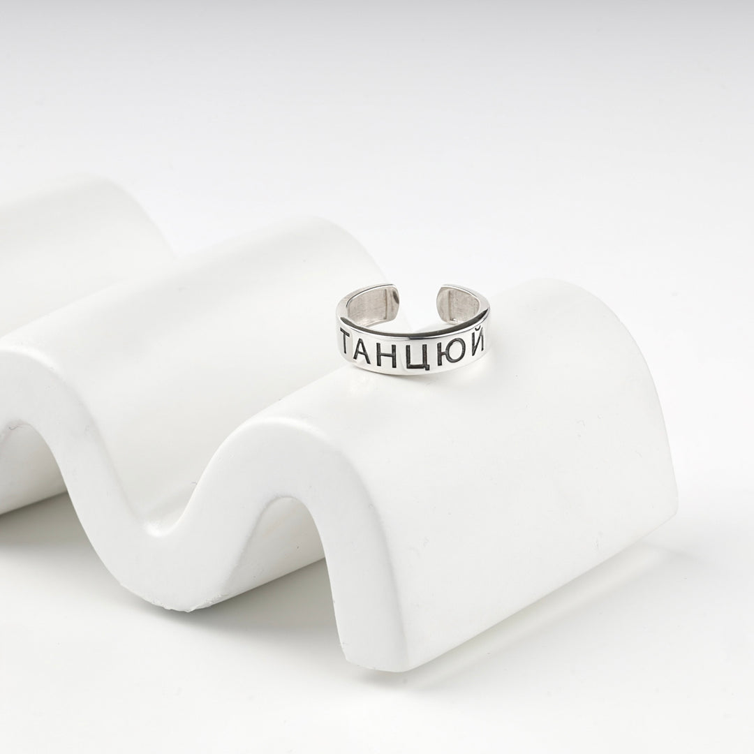 Engraved silver ring resting on a white wave display