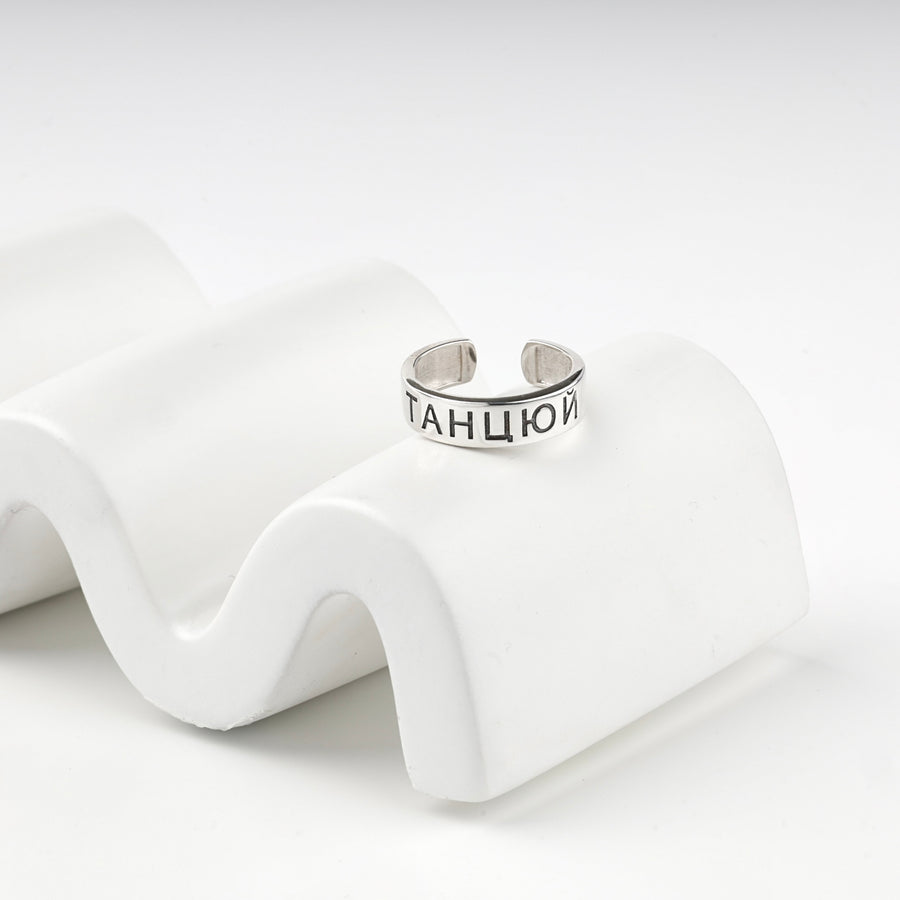 Engraved silver ring resting on a white wave display