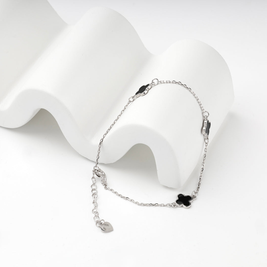 Silver 925 clover bracelet draped over a white wave-shaped display block