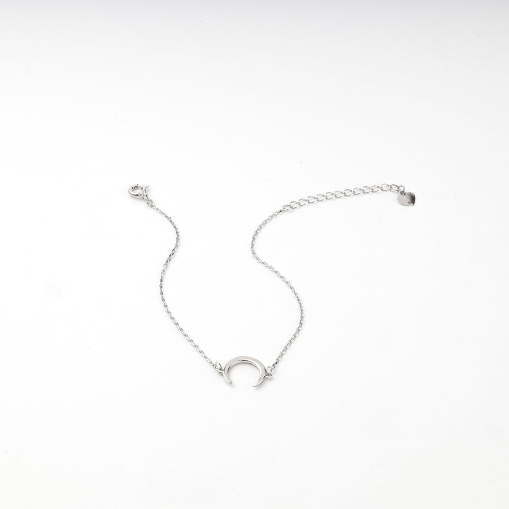 Silver 925 crescent moon bracelet draped over a white wave-shaped display block