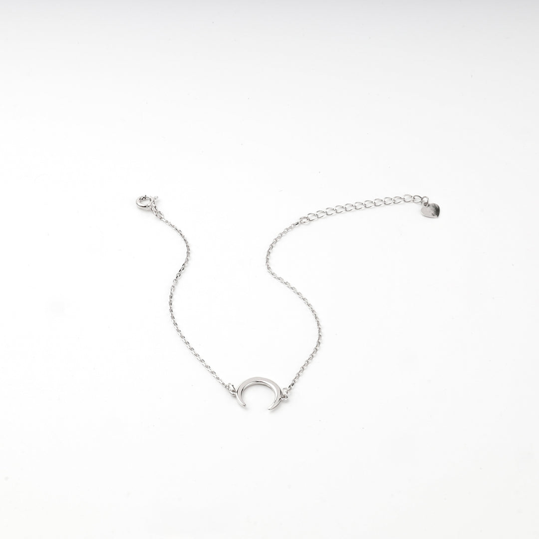 Silver 925 crescent moon bracelet draped over a white wave-shaped display block