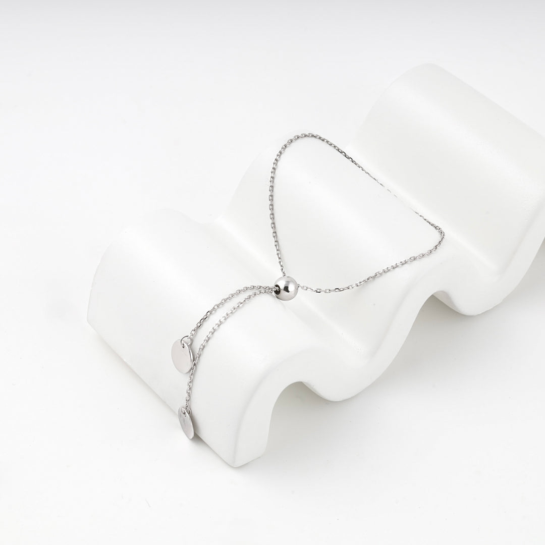 Silver 925 bolo bracelet with disc charms draped over a white wave-shaped block
