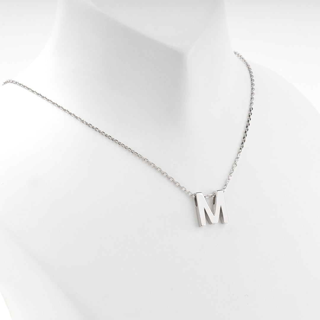 Letter M necklace worn at the base of the neck, front view