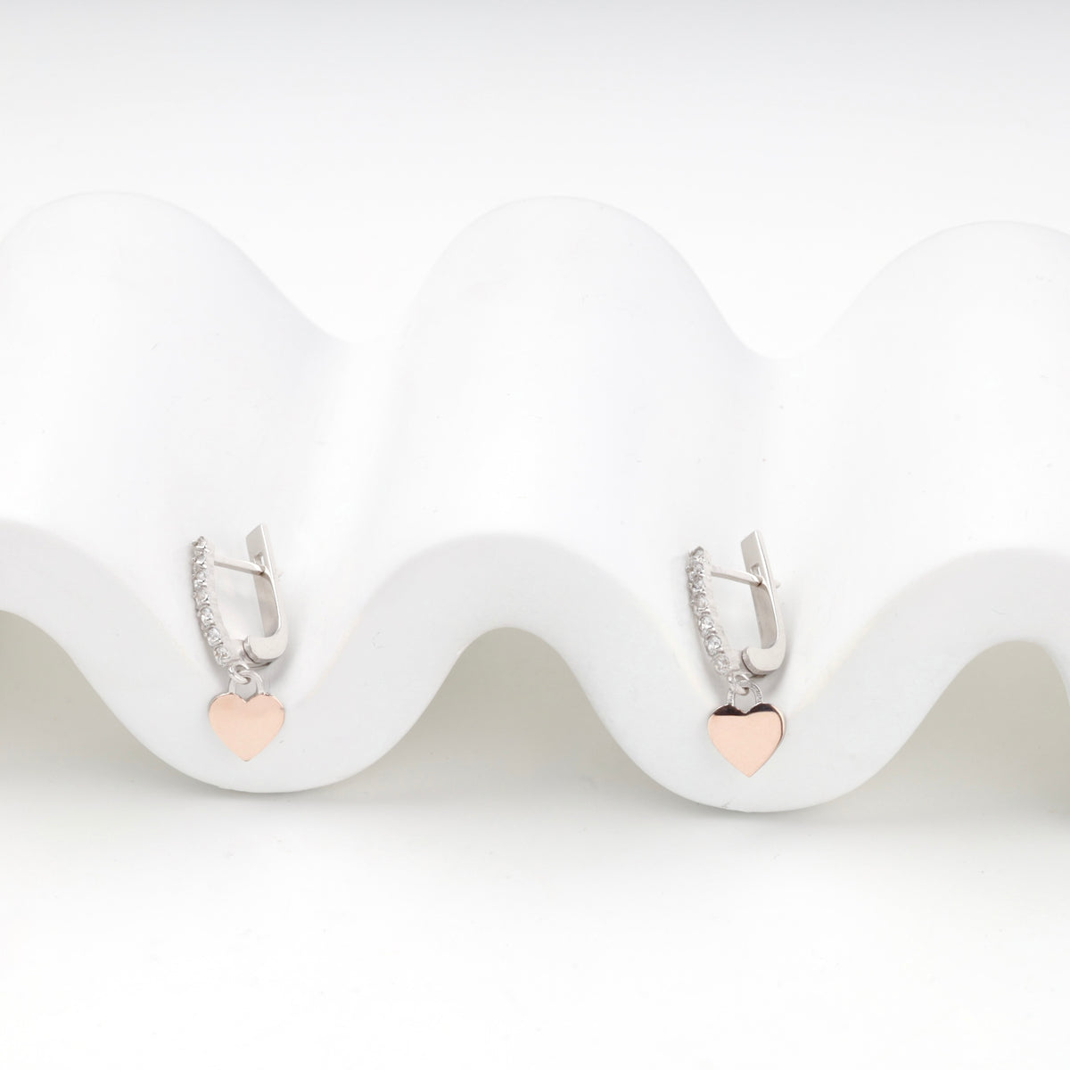Both cubic zirconia earrings resting side by side on a curved white display