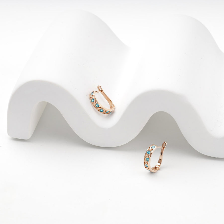 Blue cubic zirconia rose gold huggie earrings on a white stand