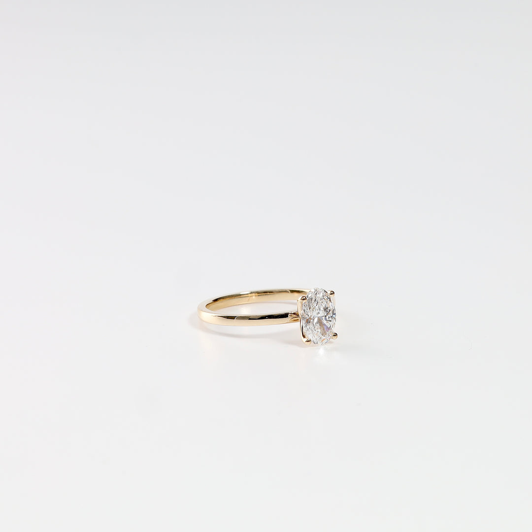 Warm 18K yellow gold oval lab-grown diamond solitaire ring on a white background, low angle.
