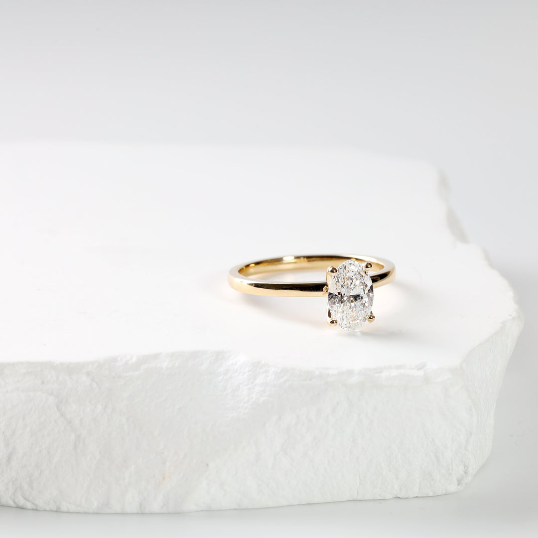 18K yellow gold oval lab-grown diamond solitaire ring upright against a white slab, through-the-band view.