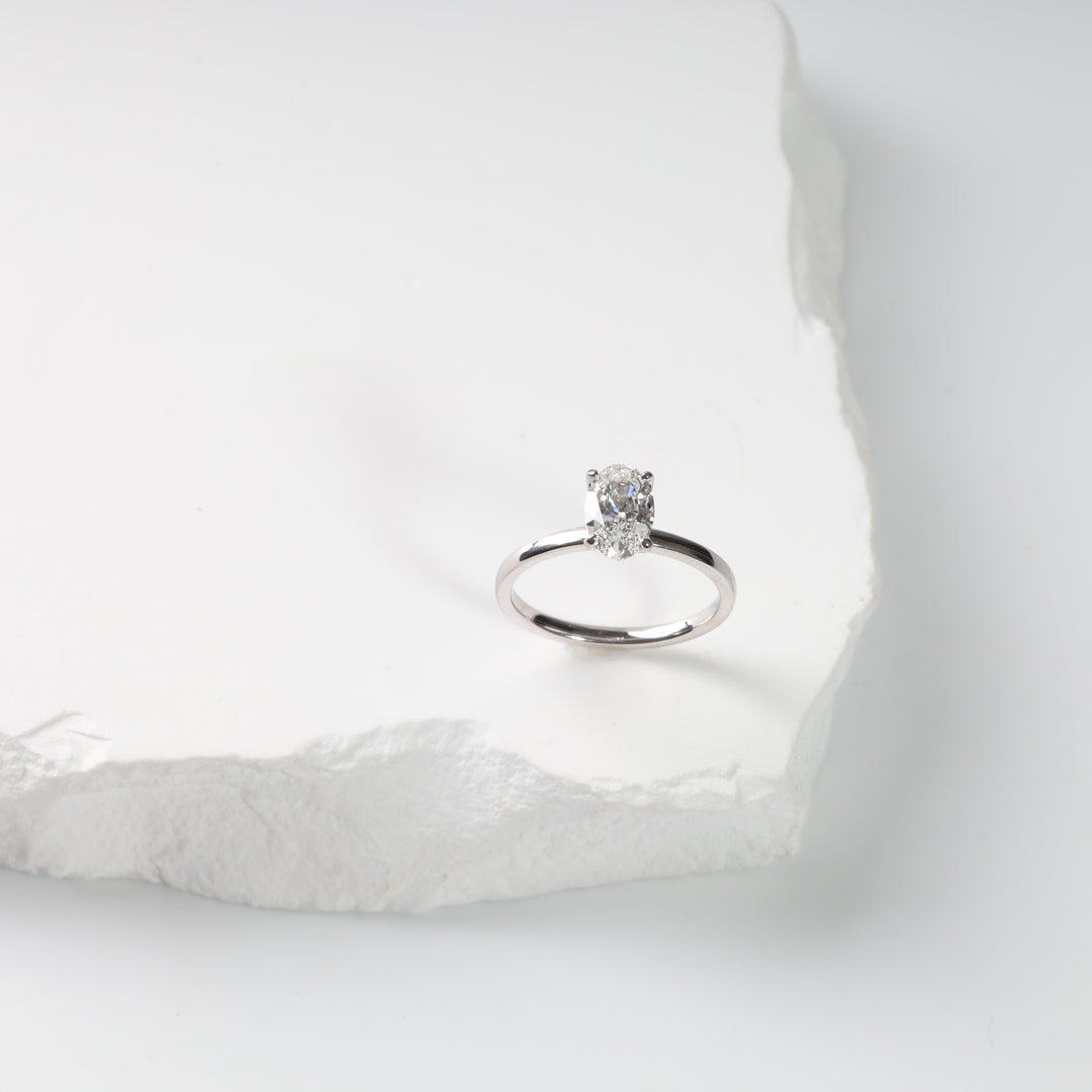 14K white gold oval lab-grown diamond ring on a white textured slab.