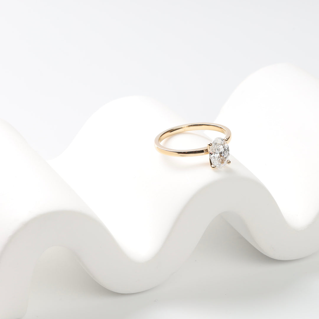 Yellow gold oval lab-grown diamond engagement ring on a white surface, angled view.