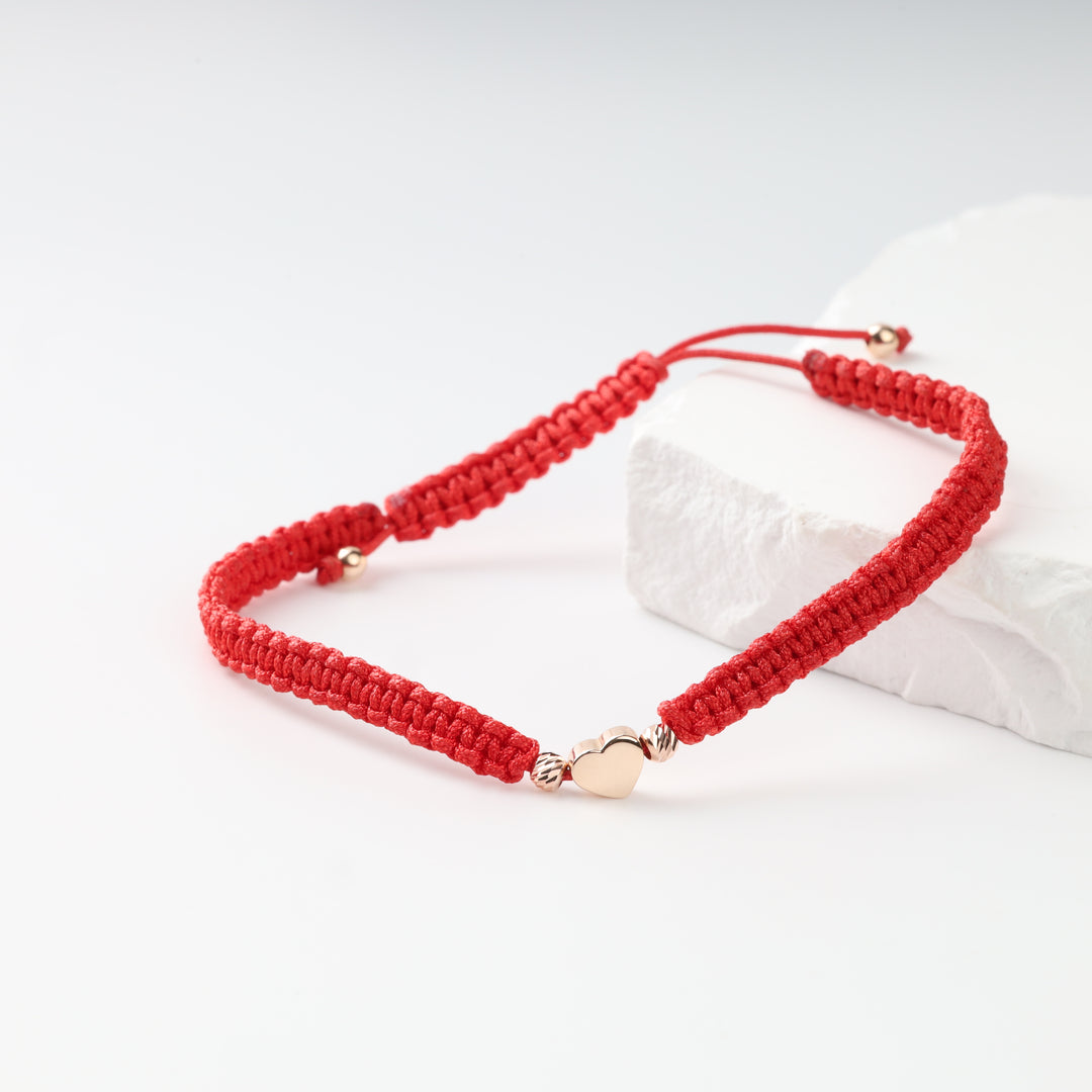 Close view of rose gold heart and faceted beads on red cord bracelet