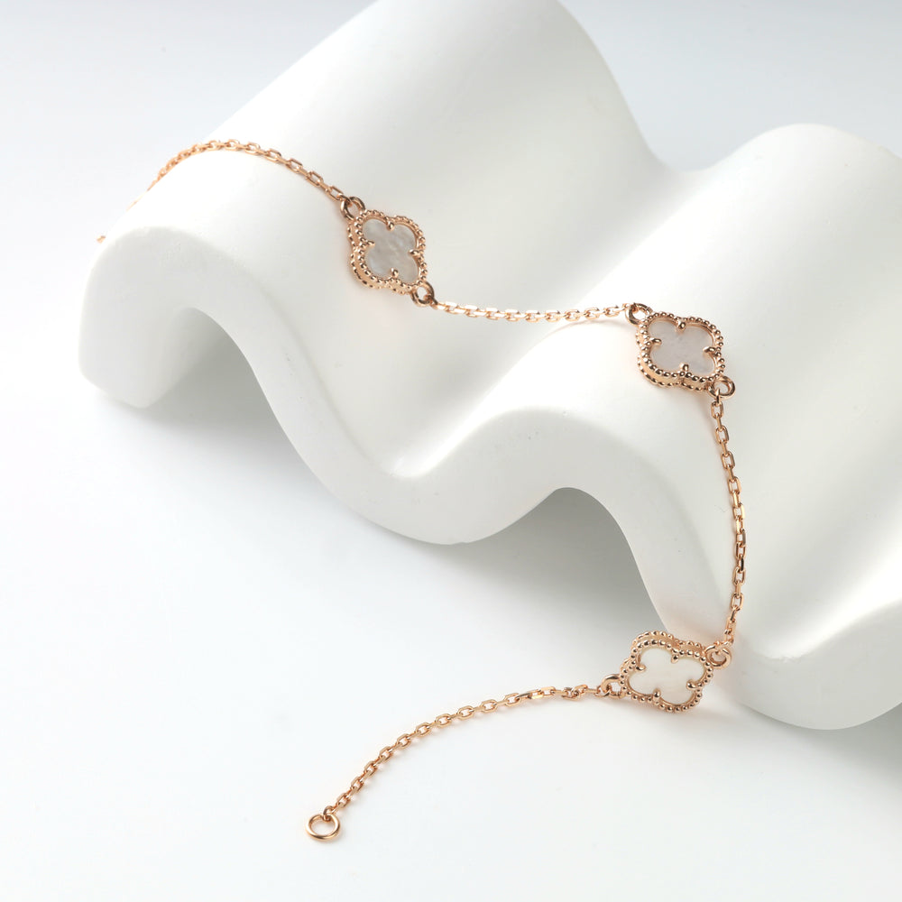 14K (585) rose gold clover bracelet draped over a white display wave