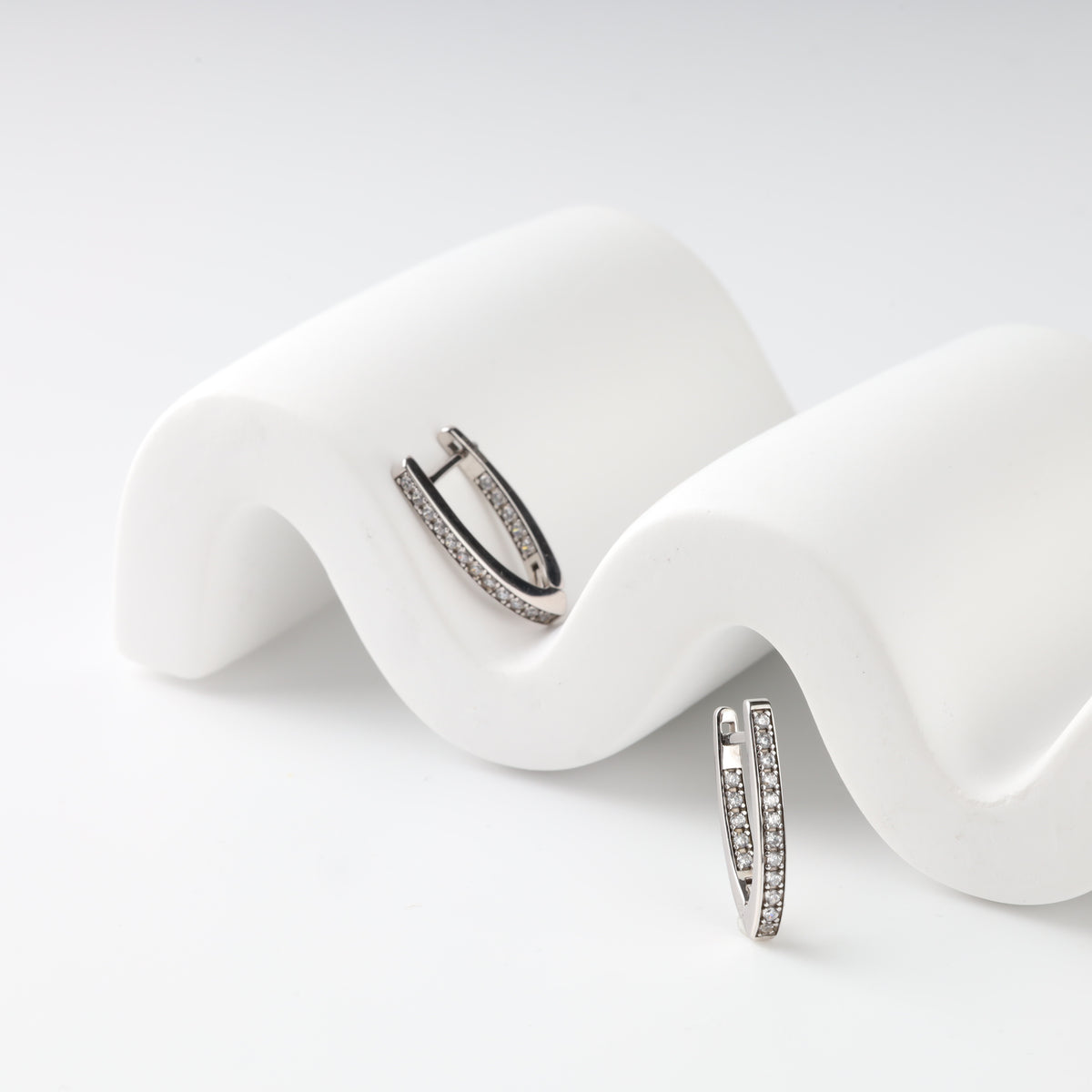 Pair of 14K (585) white gold V-shaped hoop earrings on a white wave display