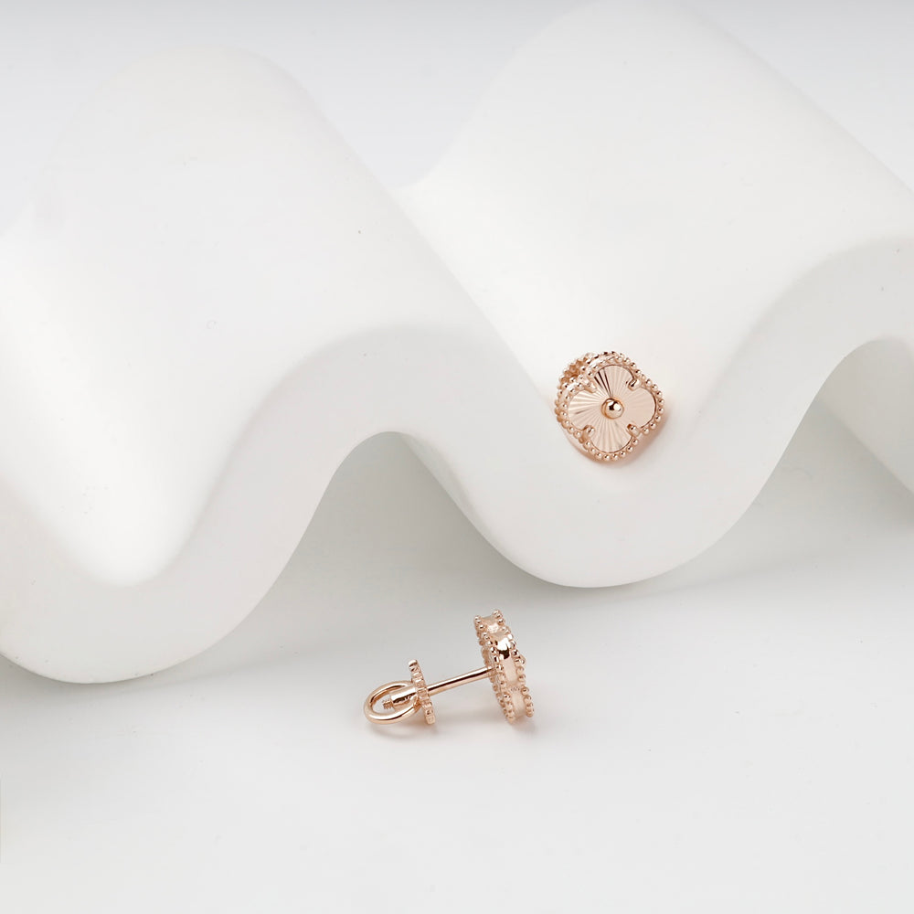 Rose gold clover stud earrings pair on white surface