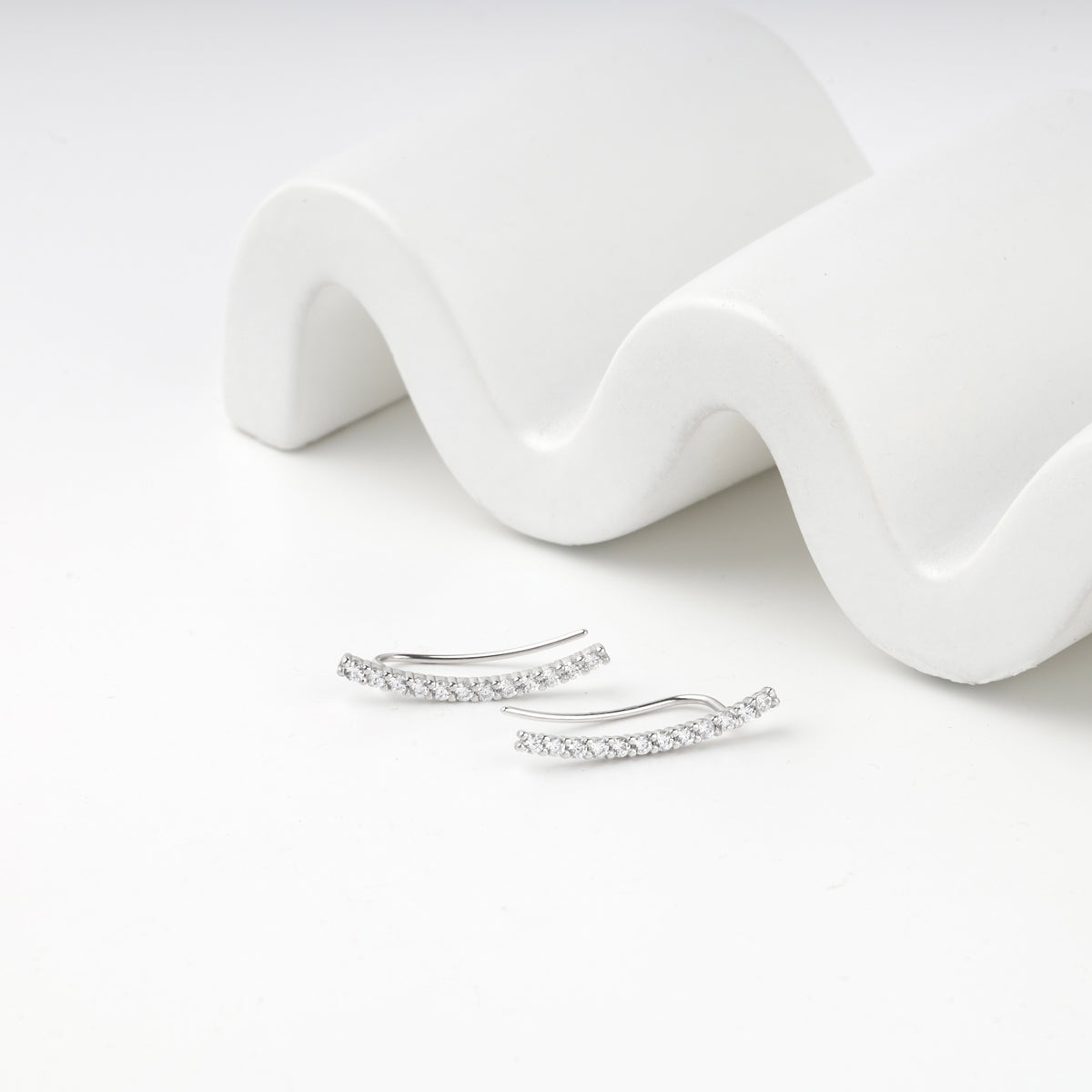 Pair of silver 925 ear climbers below a wavy white prop