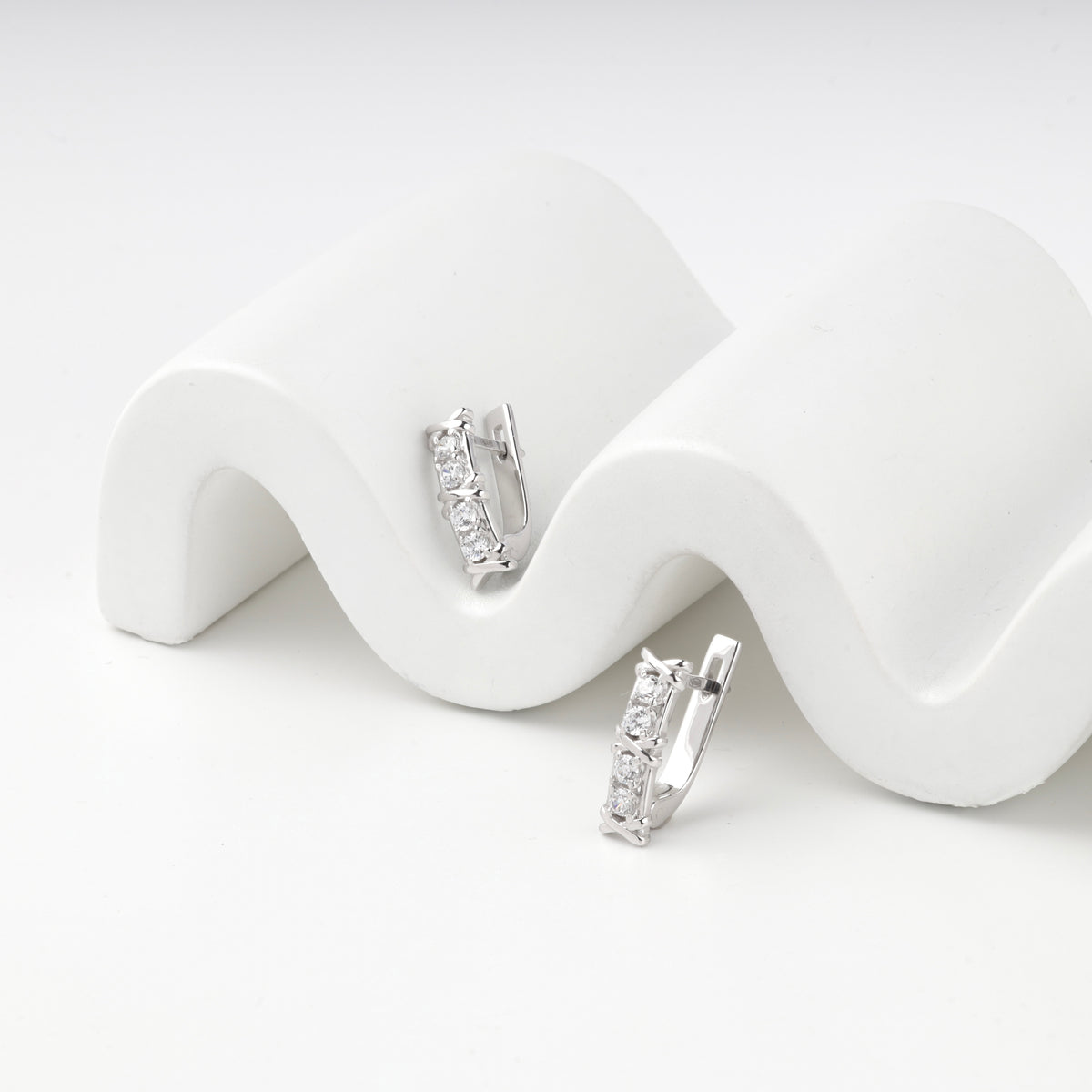 Pair of silver 925 zirconia earrings resting on a wavy white prop