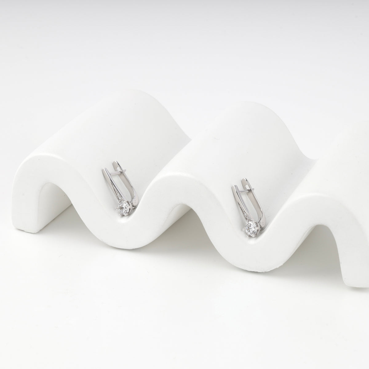 Pair of silver 925 earrings with round cubic zirconia on a wavy prop