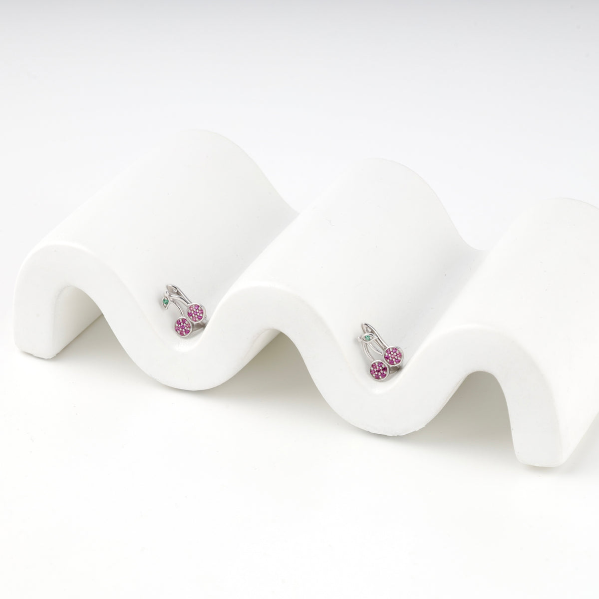 Silver 925 cherry earrings resting on a wavy white display block