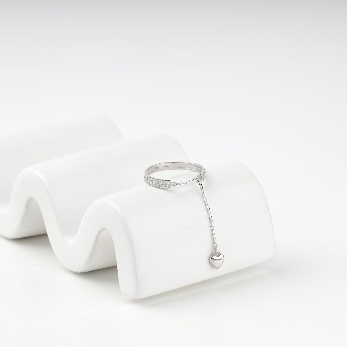 Silver 925 pave ring with its heart charm chain on a wavy white prop