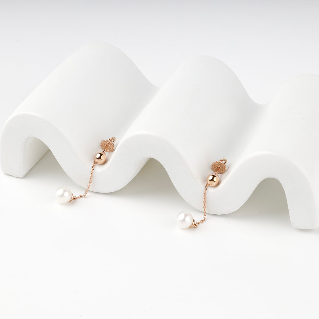Pair of rose gold 585 earrings with white pearl drops on a white wave stand