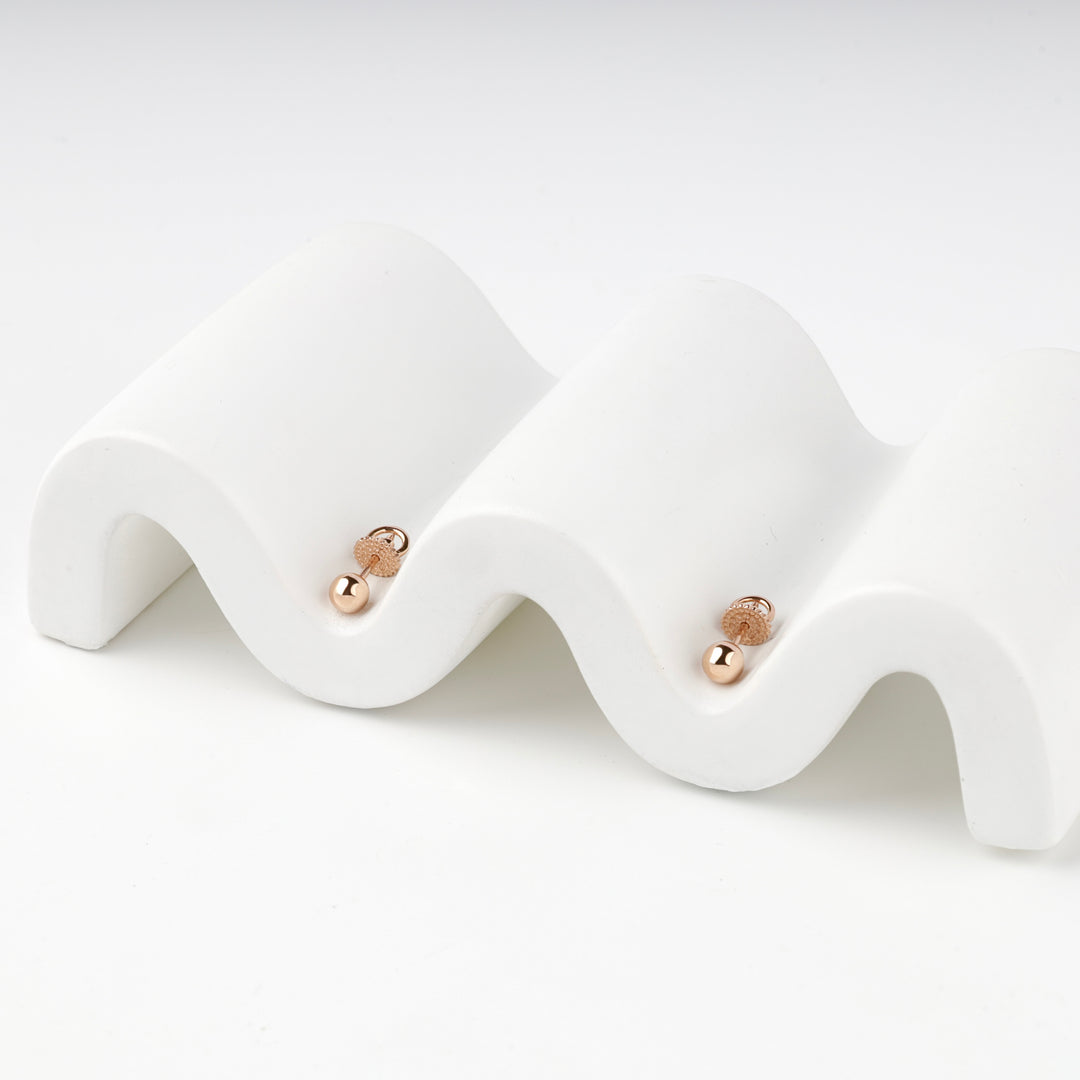 Pair of rose gold 585 ball stud earrings with screw backs on a white wave stand