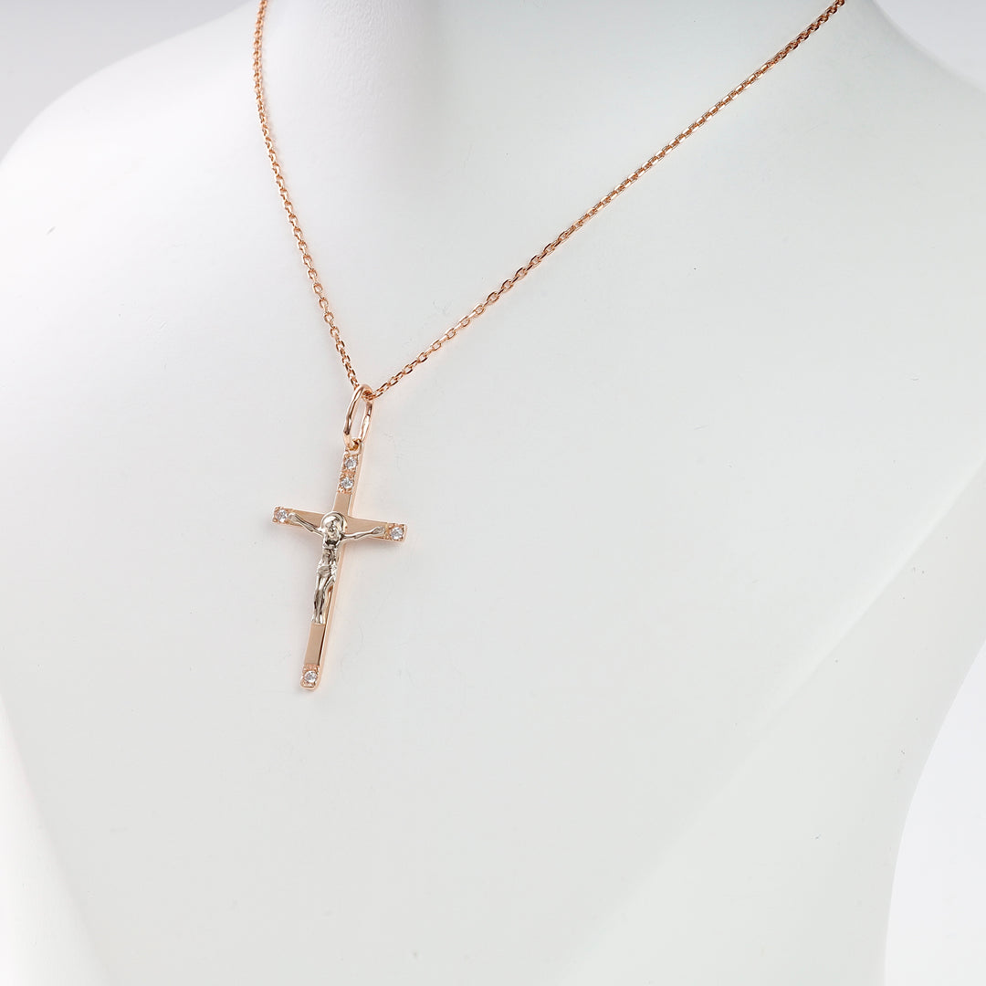 Rose gold crucifix pendant necklace with a figure of Jesus and clear stones, displayed on a white mannequin bust.