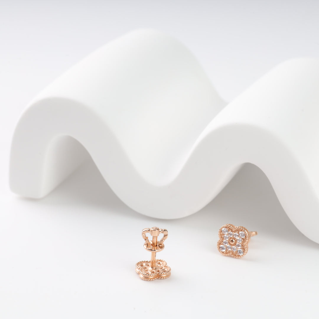 Gold floral stud earrings with clear gemstones displayed on a white wavy background.