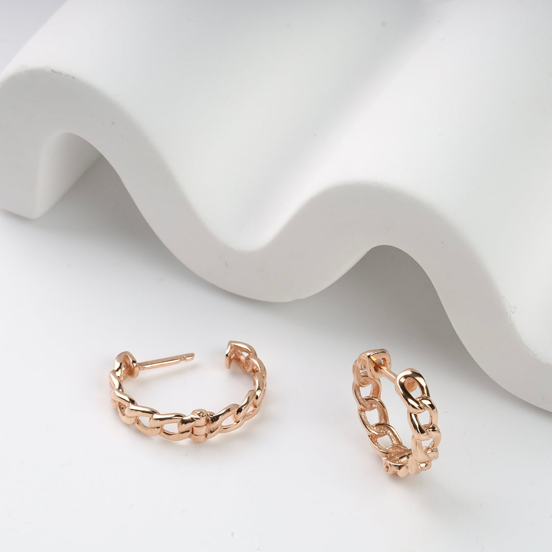 Rose gold chain link hoop earrings on a white wavy background.