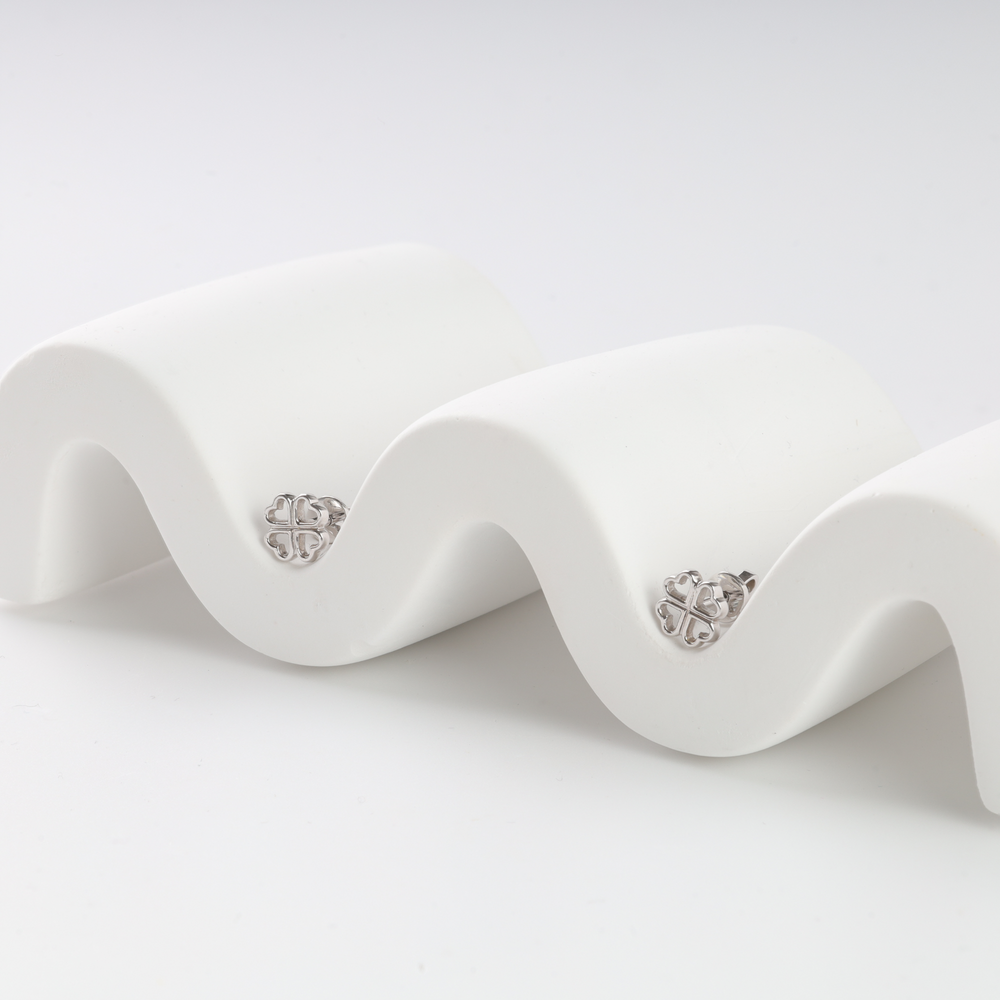 Pair of silver clover stud earrings with heart-shaped leaves displayed on a white wavy stand.
