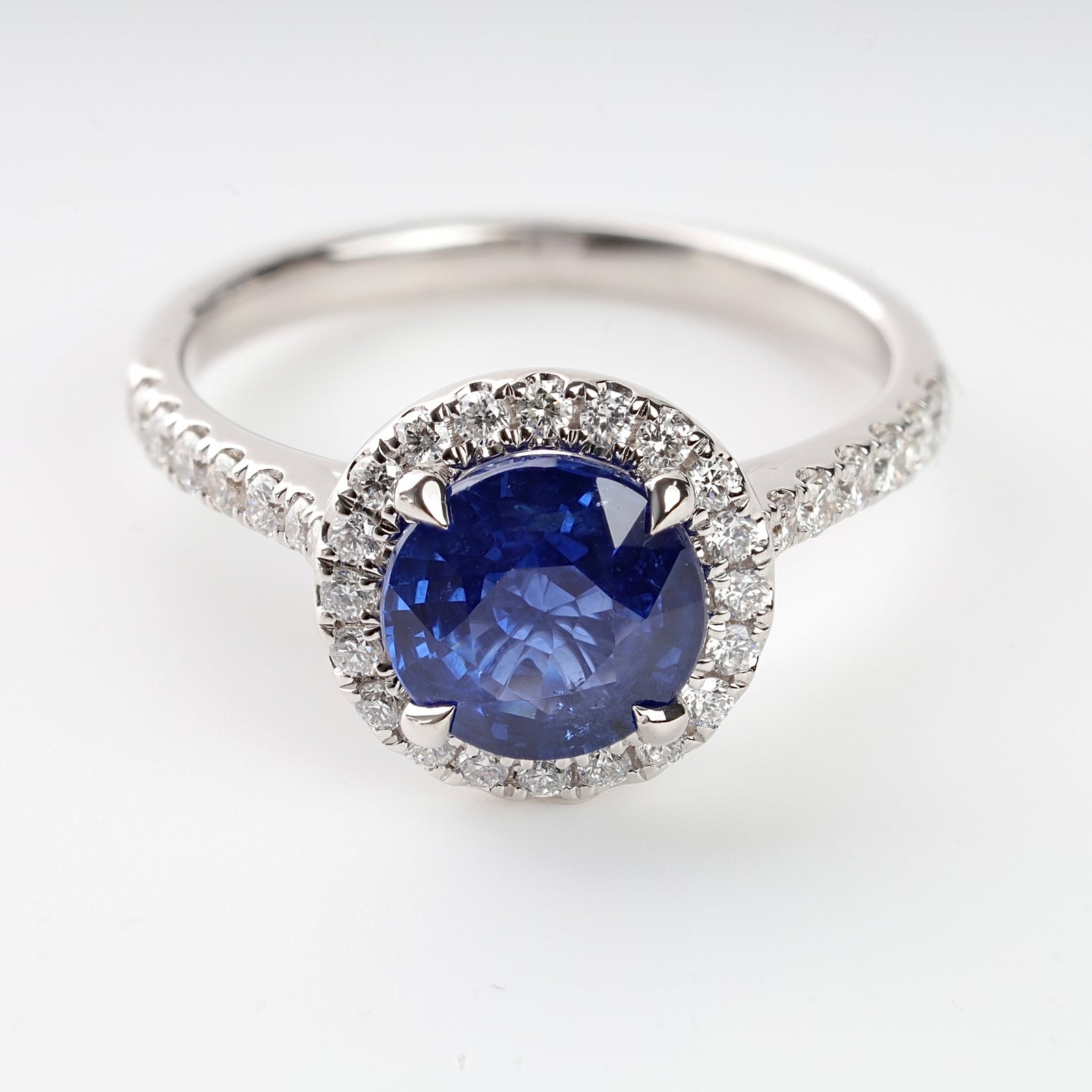 White gold ring with a round blue sapphire center stone and a halo of small diamonds, displayed on a white background.