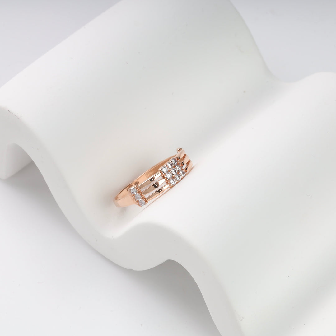 Rose gold ring with geometric cubic zirconia accents on a wavy white surface.