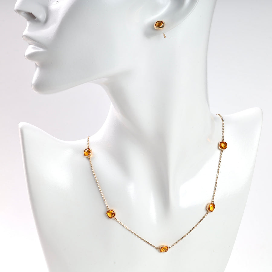 Gold chain necklace and stud earring with amber gemstones displayed on white mannequin.