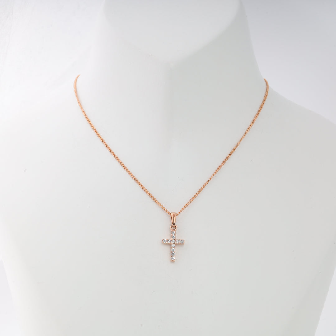 Rose gold chain necklace with a small cross pendant encrusted with clear gemstones on a display bust.