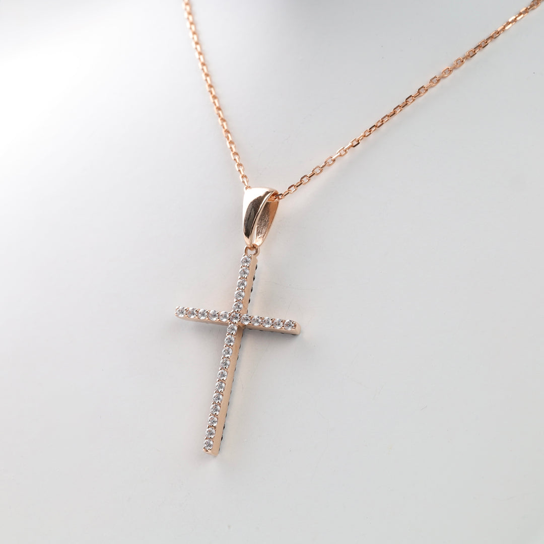 Rose gold chain with a cross pendant adorned with small diamonds on a white background.
