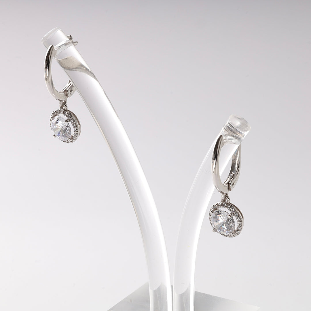 Silver hoop drop earrings with round clear crystal pendants displayed on a white stand.