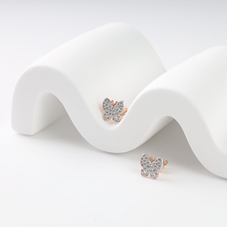 Gold butterfly earrings with clear crystals on a white wavy stand.