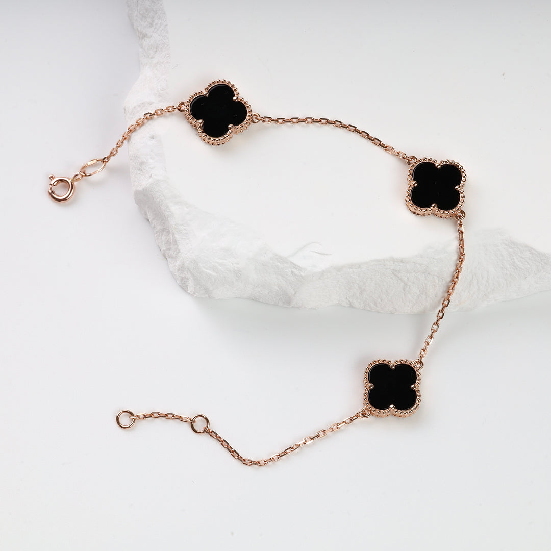Gold chain bracelet with three black enamel clover charms displayed on a white surface.