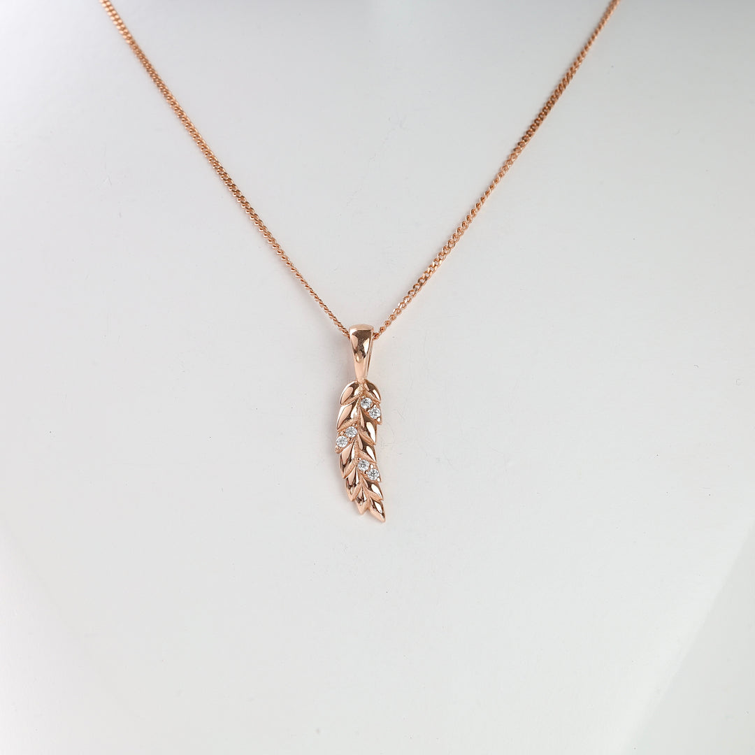 Rose gold necklace with a leaf-shaped pendant and small clear stones displayed on a white bust.