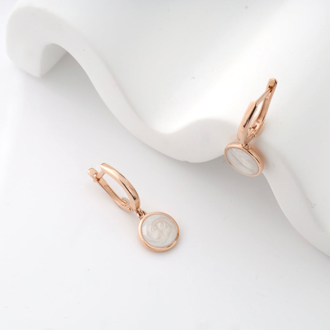 Rose gold hoop earrings with round white enamel pendants displayed on a white background.