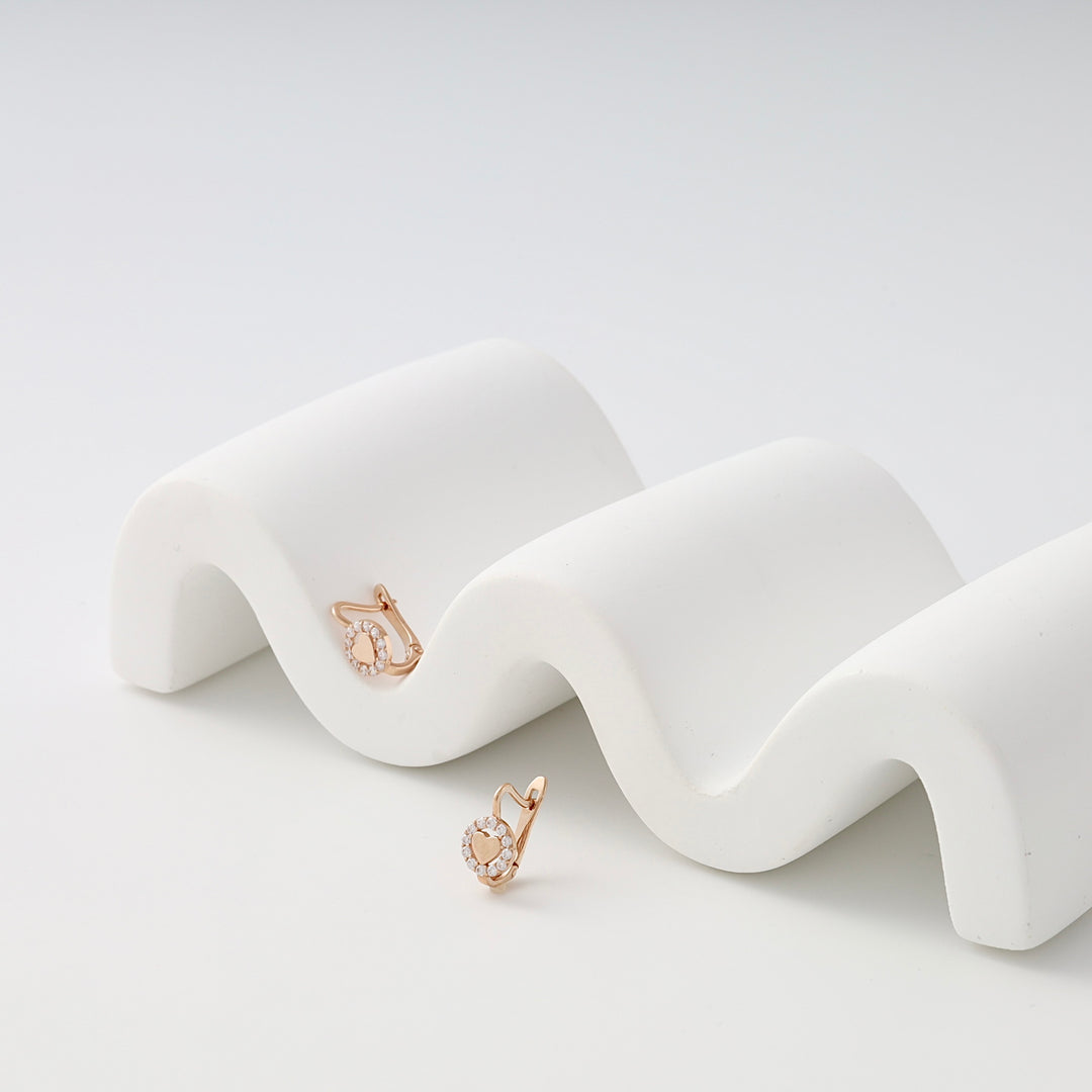 Rose gold kids earrings with round cubic zirconia stones displayed on a white wavy stand.