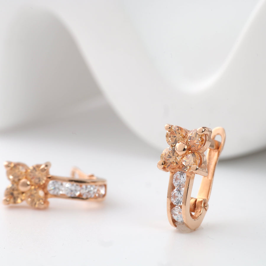 Rose gold floral and crystal huggie earrings with clear stones displayed on a white background.