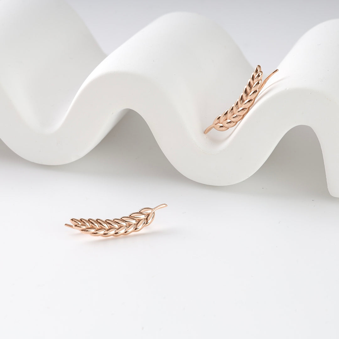 Pair of rose gold ear climber earrings with leaf motif displayed on a white wavy stand.