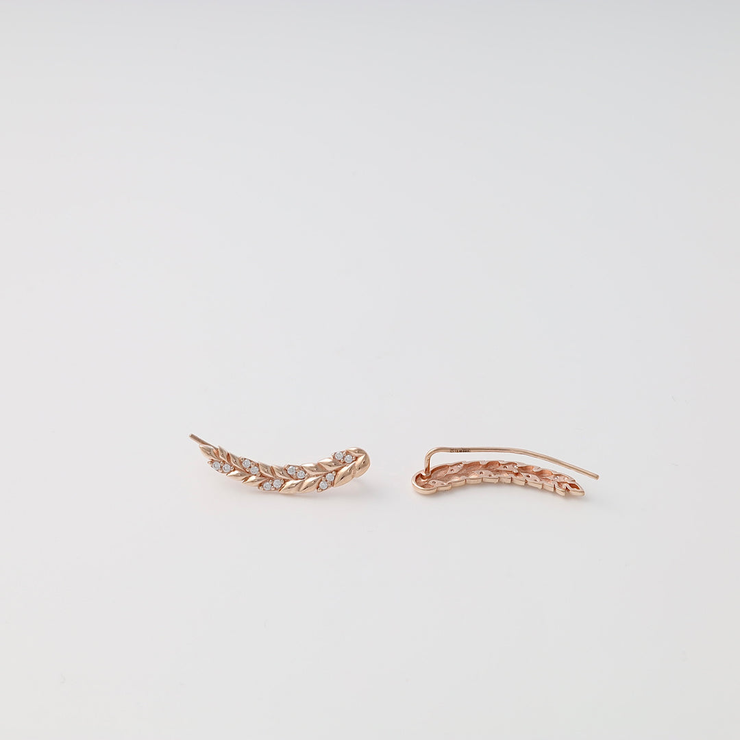 Pair of rose gold ear climber earrings with leaf design and clear stones on a white background.
