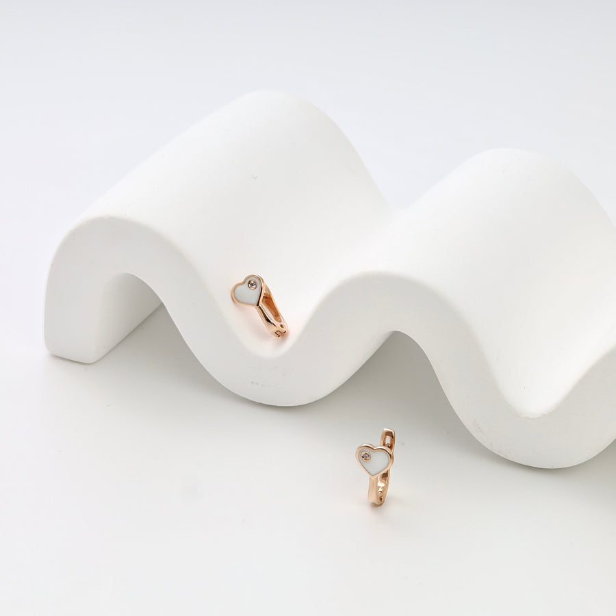 Rose gold heart huggie earrings with white enamel and tiny stone studs on white display, Ukrainian Jewelry, dainty gold earrings.