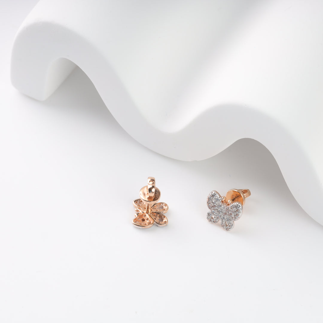 Two butterfly stud earrings with rose gold and diamond accents on a white surface.