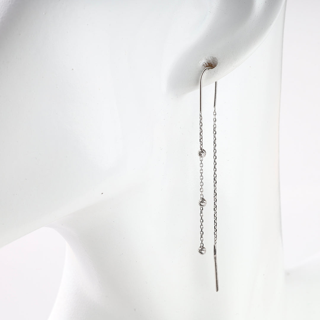 Single silver threader earring with a delicate chain and small knot details on a white mannequin display.