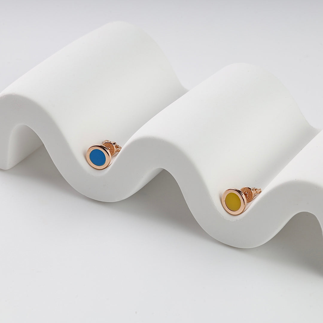 Pair of gold stud earrings with blue and yellow enamel circles displayed on a wavy white stand.